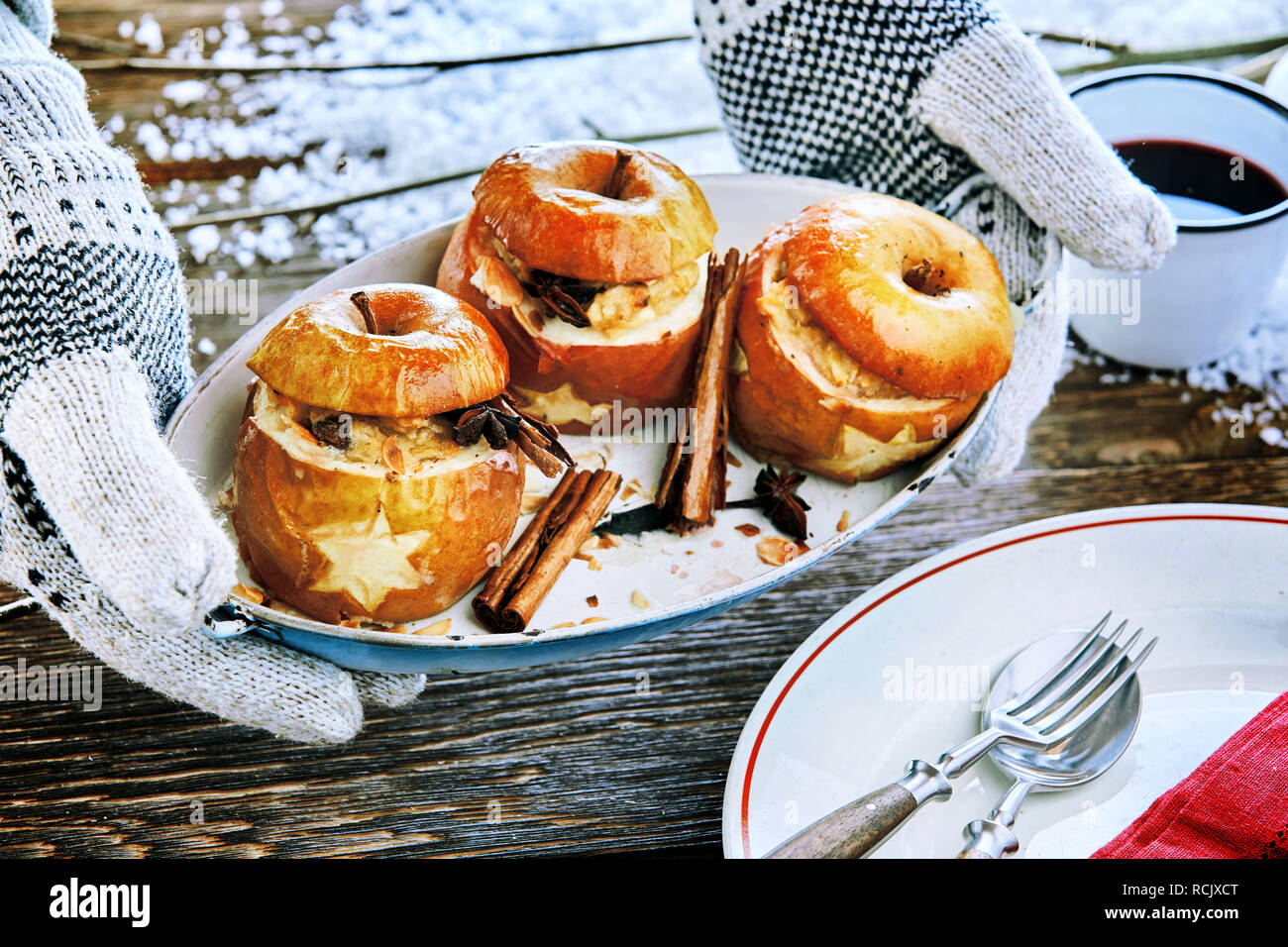 Mani guantate tenendo una lastra di cotto al forno ripiene di mele speziate con cannella sopra un tavolo nevoso a un inverno outdoor barbecue a Natale Foto Stock