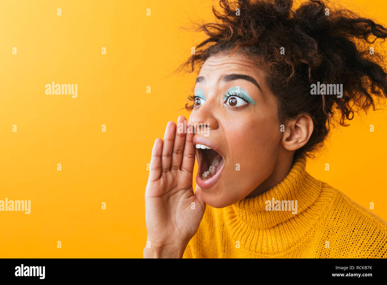 Ritratto di entusiasti americano africano donna con acconciatura afro urlando o richiamo permanente, mentre isolate su sfondo giallo Foto Stock