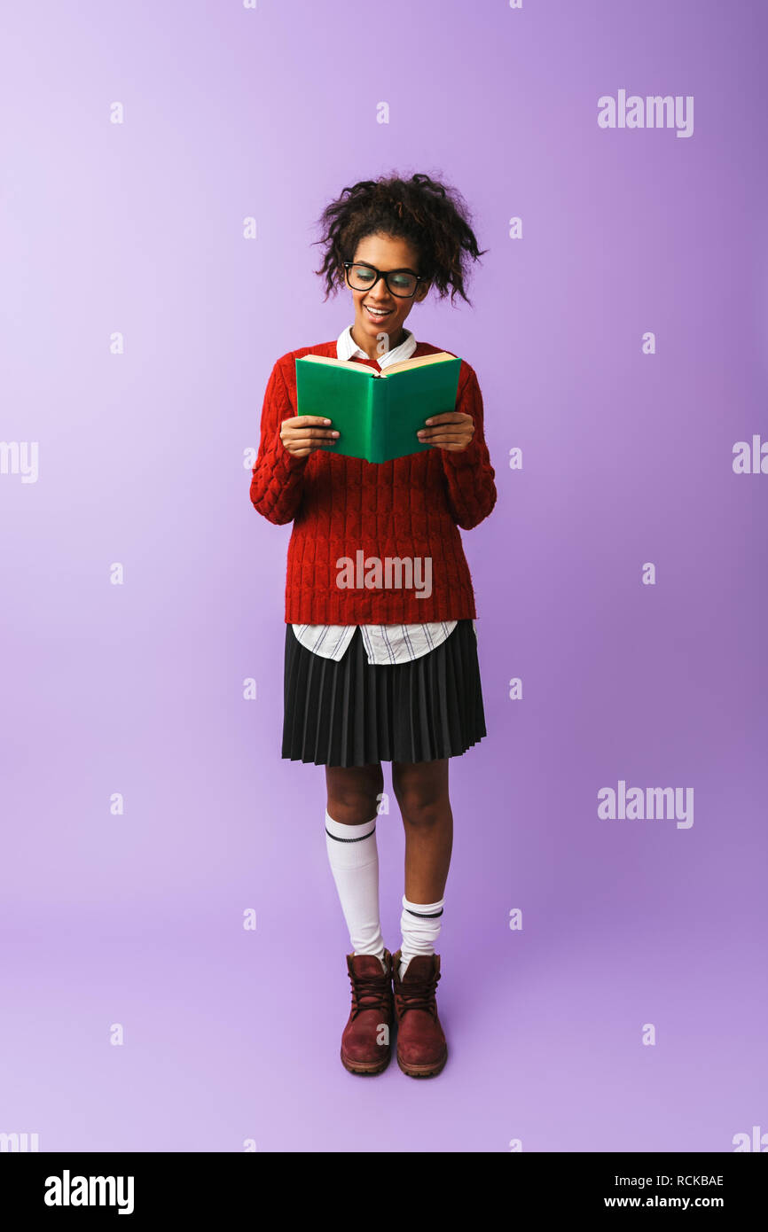 African American teenage donna in uniforme scolastica holding e la lettura prenota isolate su sfondo viola Foto Stock