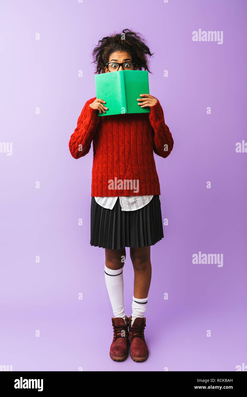 African American giovane donna in uniforme scolastica holding e la lettura prenota isolate su sfondo viola Foto Stock