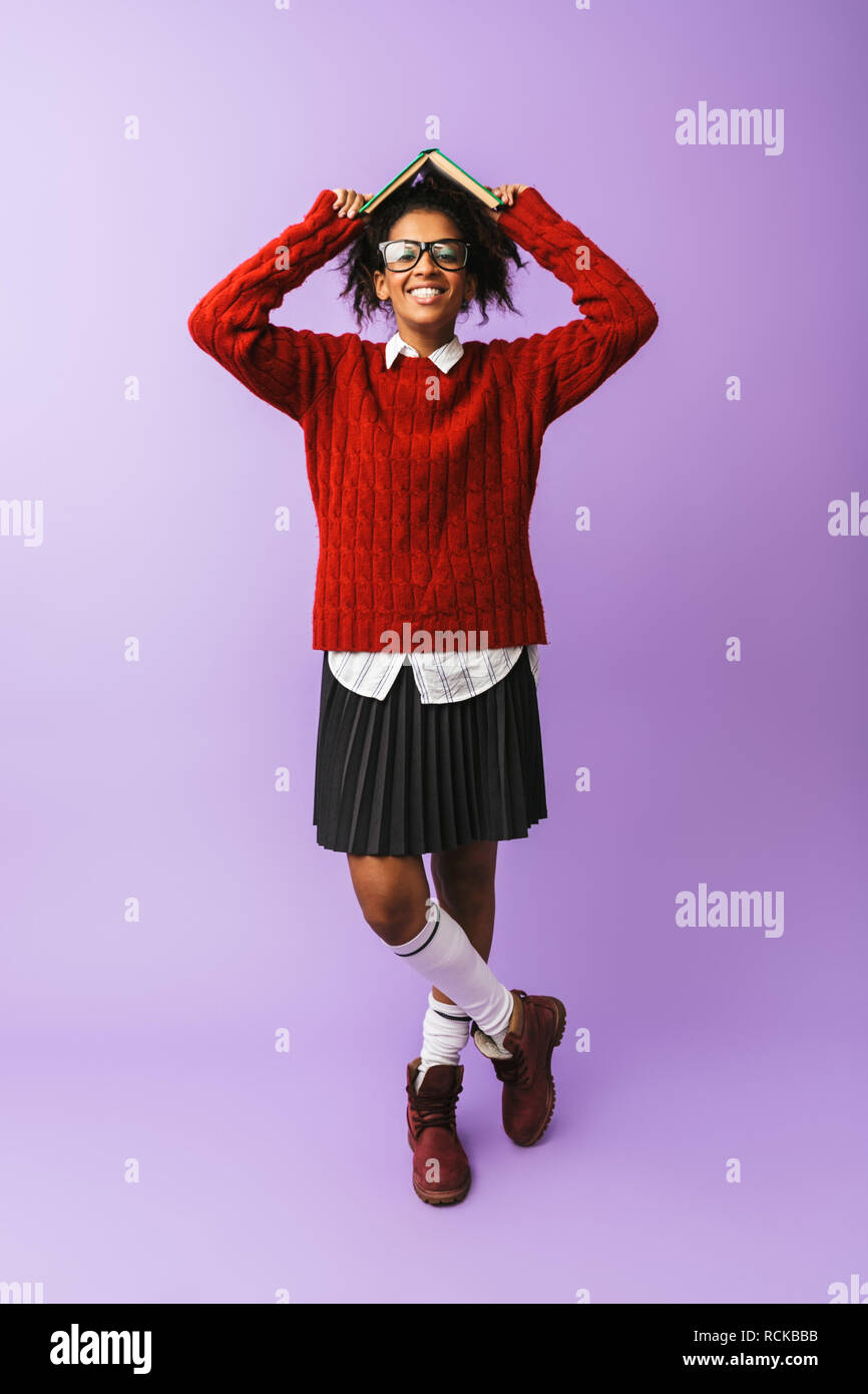 Americano africano ragazza eccitato in uniforme scolastica azienda prenota isolate su sfondo viola Foto Stock