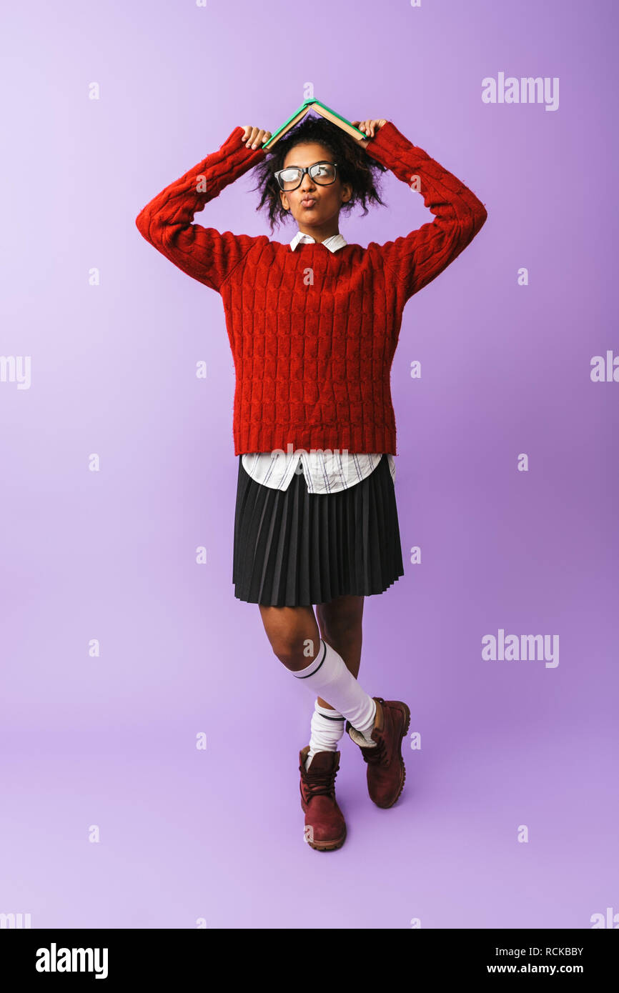 African American brunette girl in uniforme scolastica azienda prenota isolate su sfondo viola Foto Stock