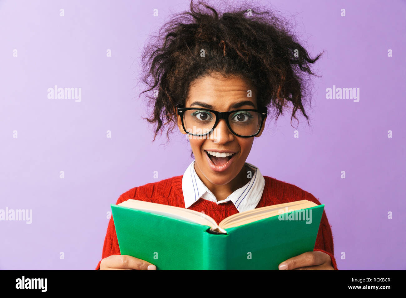 African American smart studente in uniforme di contenimento e la lettura di libro isolato su sfondo viola Foto Stock