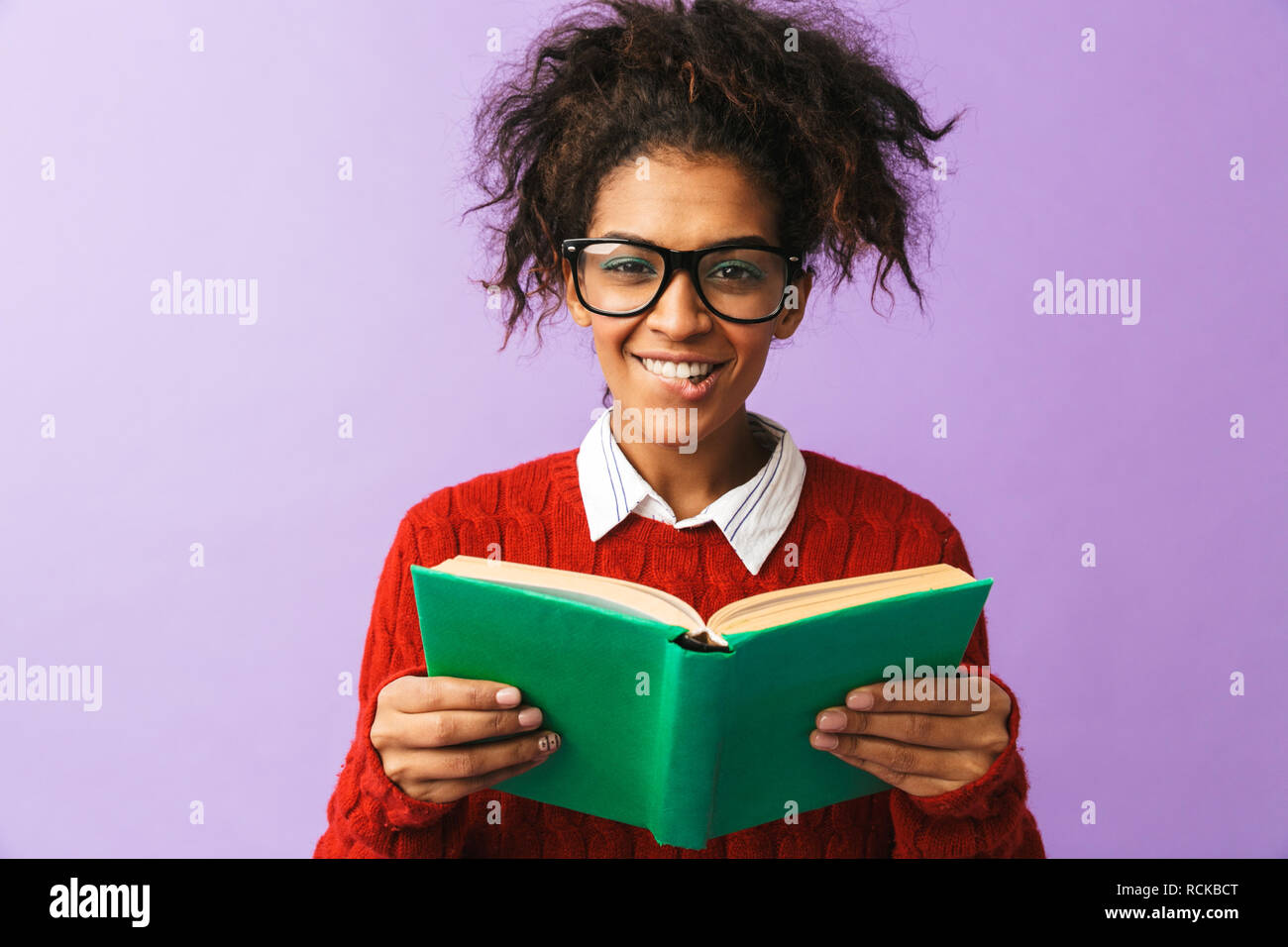 African American felice studente in uniforme di contenimento e la lettura di libro isolato su sfondo viola Foto Stock