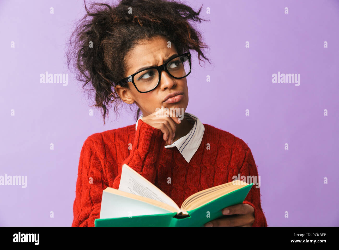 African American smart donna in uniforme scolastica holding e la lettura prenota isolate su sfondo viola Foto Stock