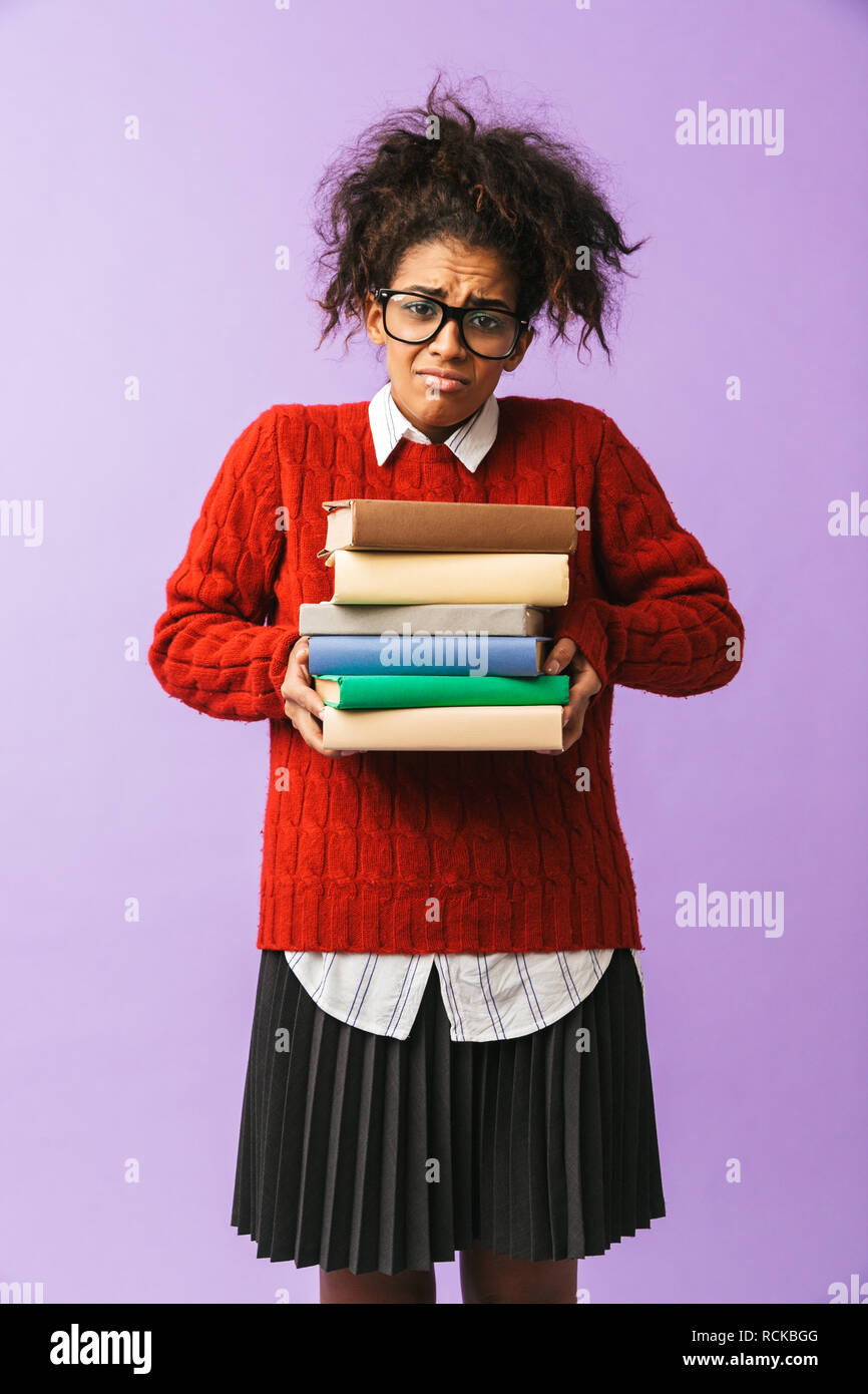 Americano africano ragazza adolescente in uniforme scolastica tenendo il mazzo di libri isolate su sfondo viola Foto Stock