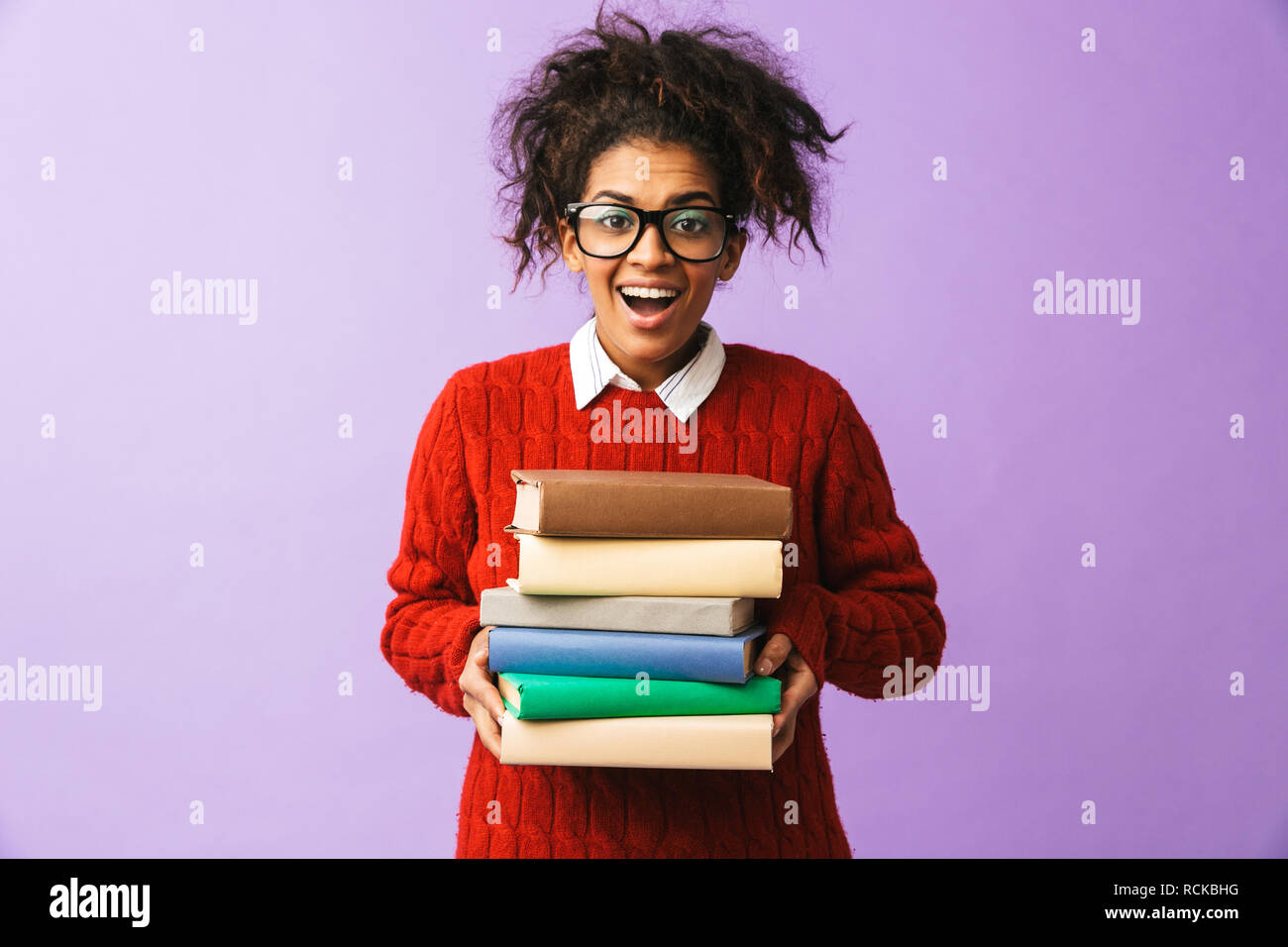 Americano africano ragazza sorridente in uniforme scolastica tenendo il mazzo di libri isolate su sfondo viola Foto Stock