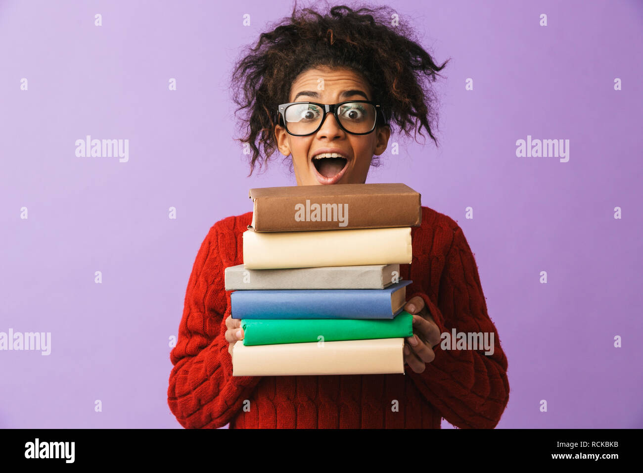 African American allegro ragazza in uniforme scolastica tenendo il mazzo di libri isolate su sfondo viola Foto Stock