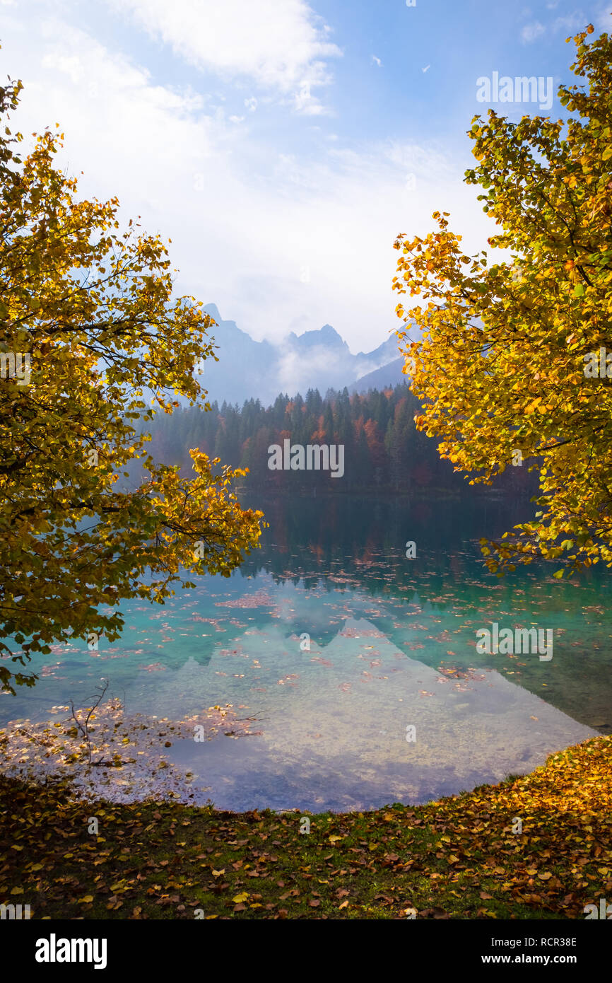 Vista sul lago di Laghi di Fusine all mountain range Mangart vicino a Tarvisio in Italia su una mattina di sole con alcune nuvole e nebbia in autunno Foto Stock