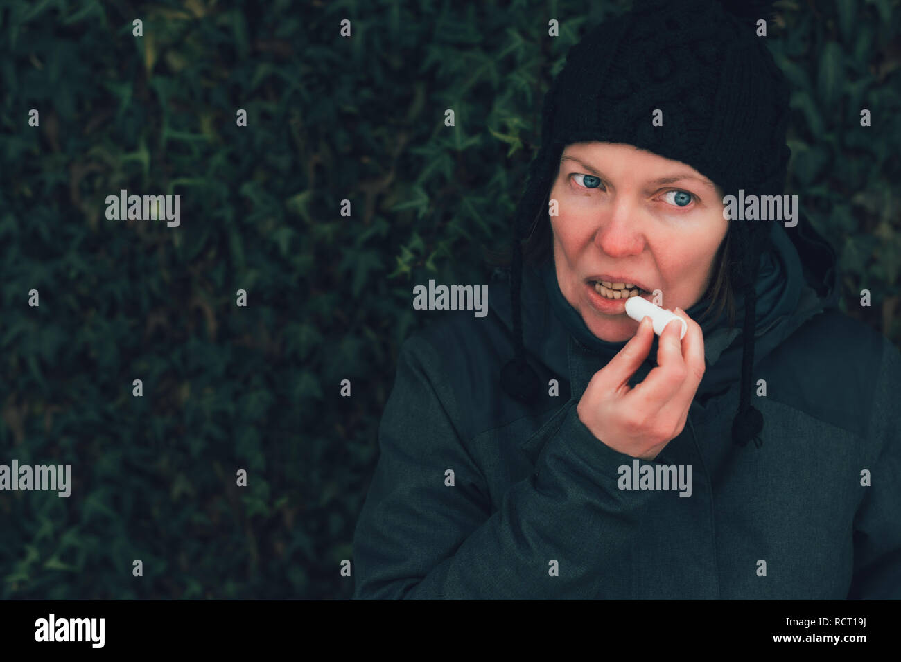 Donna applicando balsamo per labbra in fuori strada in una fredda giornata invernale contro la comune parete di edera Foto Stock