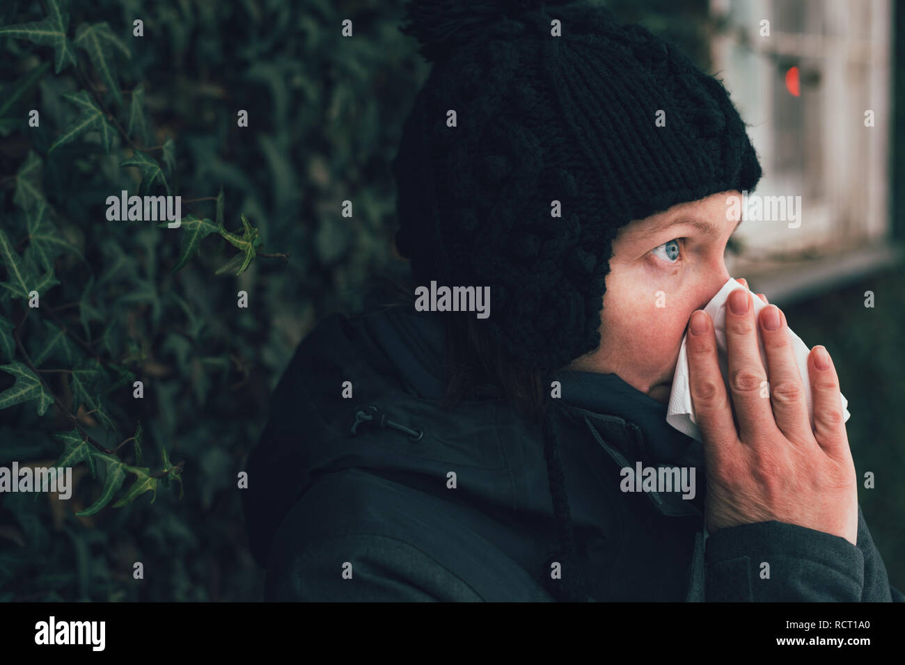 Donna soffia il naso in un fazzoletto di carta per strada in una fredda giornata invernale all'inizio della stagione influenzale Foto Stock