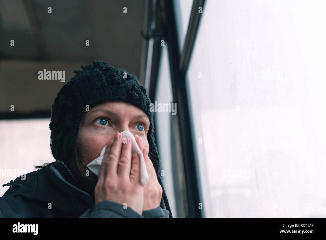 Donna soffia il naso in un fazzoletto di carta sul bus in una fredda giornata invernale all'inizio della stagione influenzale Foto Stock