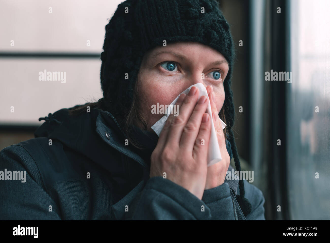 Donna soffia il naso in un fazzoletto di carta sul bus in una fredda giornata invernale all'inizio della stagione influenzale Foto Stock