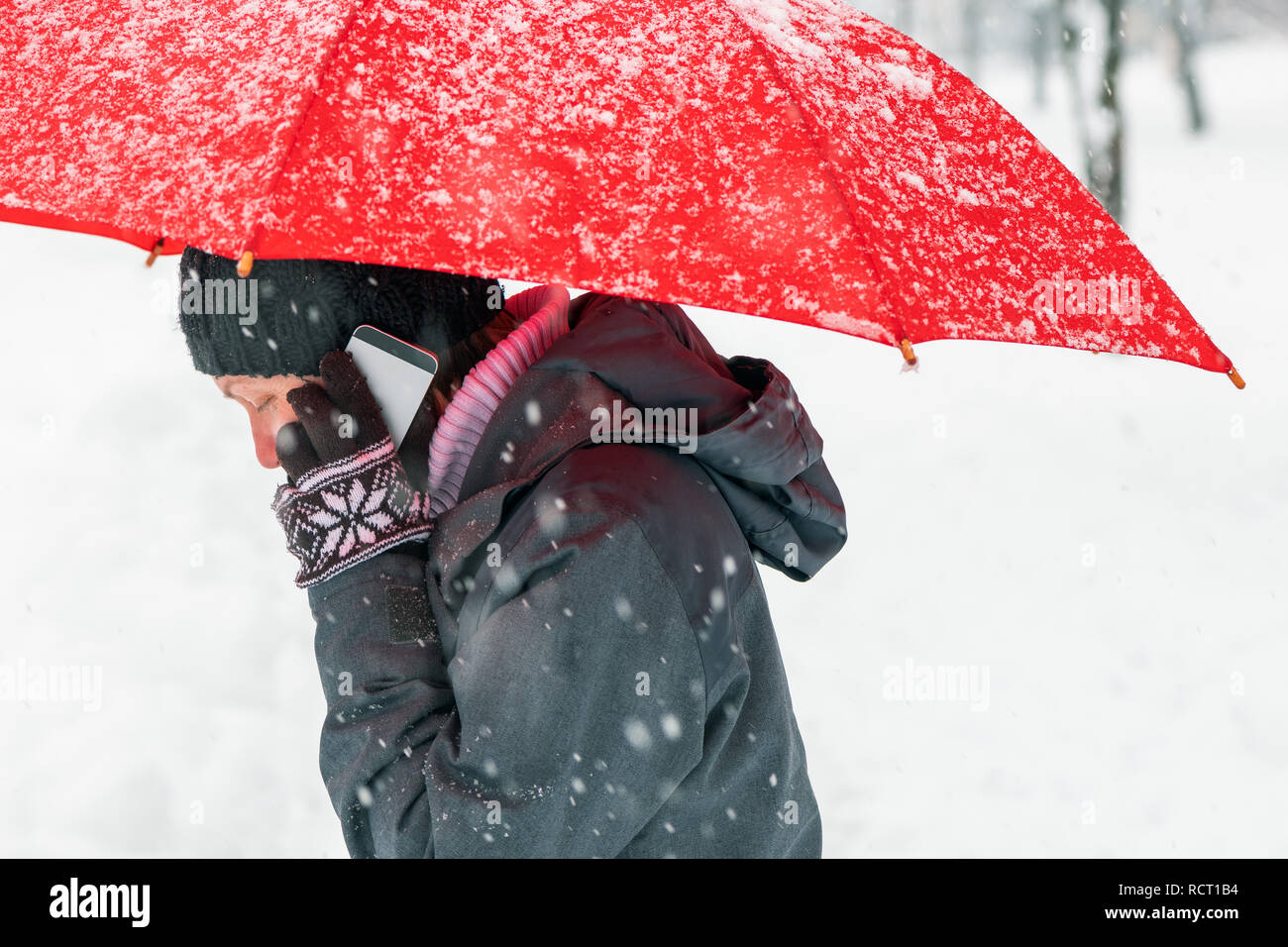 Preoccupato della donna parlando al telefono cellulare in snow all'aperto sotto ombrellone rosso Foto Stock