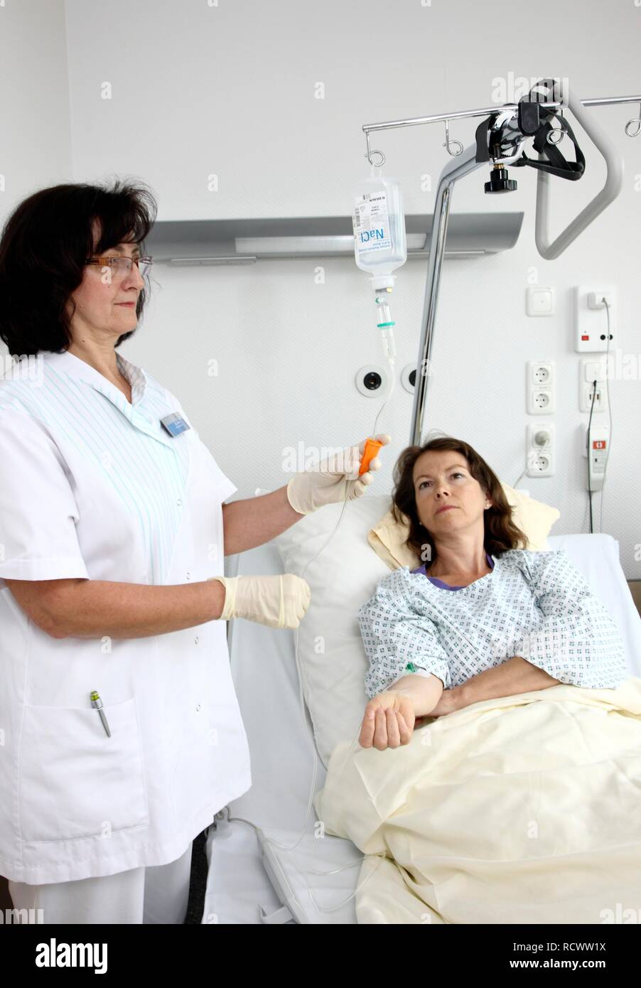 L'infermiera mettendo un paziente in un letto di ospedale su una infusione a gocciolamento, ospedale Foto Stock