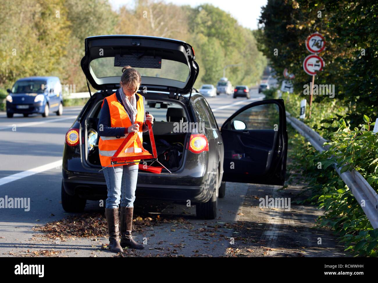 Ripartizione per auto, femmina driver sul ciglio di una strada di campagna, indossare un giubbotto, mettendo su un triangolo di avvertenza Foto Stock