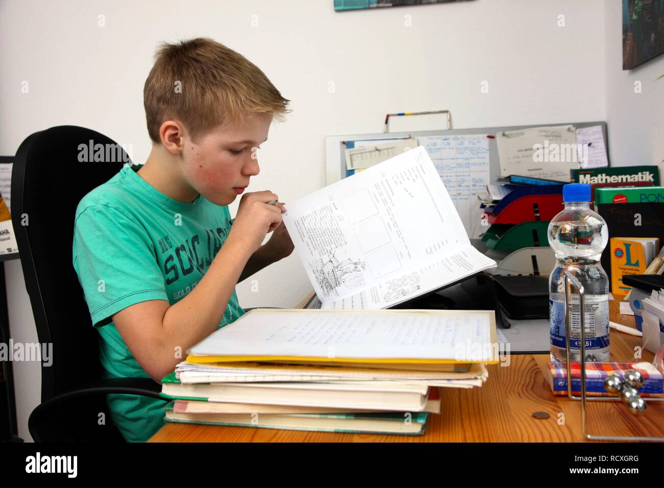 Il ragazzo, 12 anni, che sta facendo il suo dovere nella sua stanza, studiando per la scuola Foto Stock