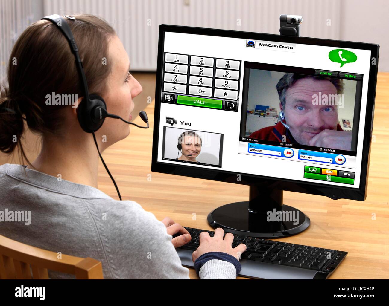 Giovane donna seduta al computer e di effettuare una chiamata via Internet, via webcam con le immagini live di entrambi Foto Stock
