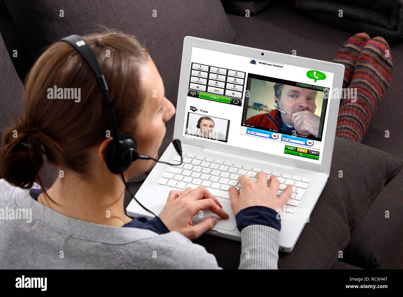 Giovane donna seduta con un computer portatile e di effettuare una chiamata via Internet, via webcam con le immagini live di entrambi Foto Stock