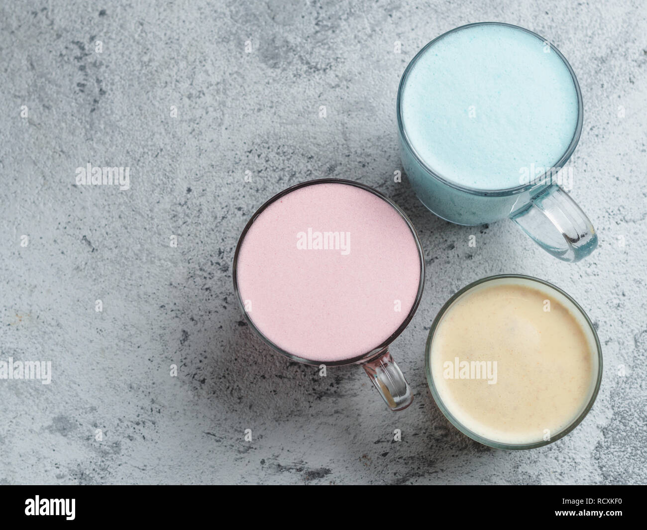 Drink alla moda: blu, giallo e rosa latte. Vista superiore della farfalla caldo pea o blue spirulina latte, giallo oro o di curcuma latte e rosa barbabietola latte sul cemento grigio Sfondo. Copia spazio per il testo Foto Stock