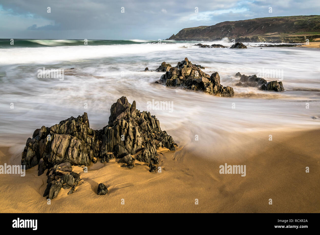 Onde sfocata turbinano intorno le rocce su una spiaggia di sabbia in Irlanda. Foto Stock