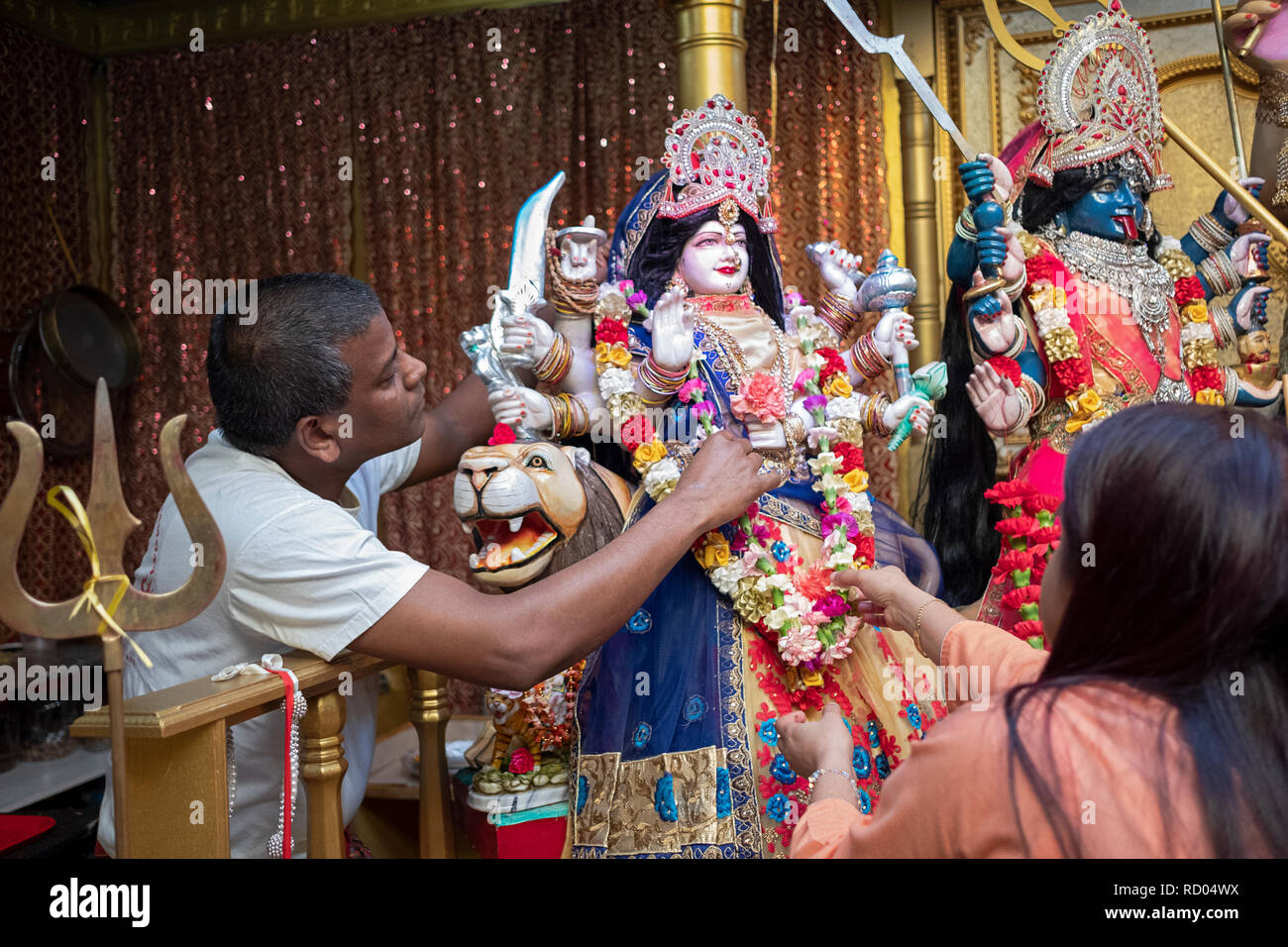 Due devoti fedeli indù decorare una statua della dea Durga con fiori. In Ozone Park, Queens, a New York. Foto Stock