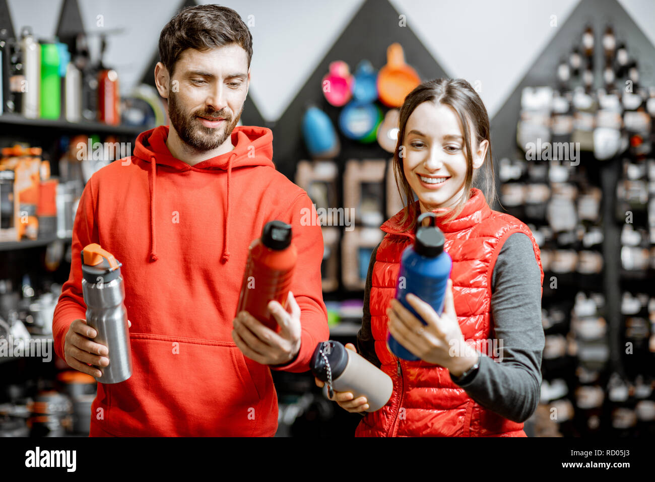 Coppia giovane vestito di rosso sportswear scelta di piatti per il campeggio in negozio con attrezzature di viaggio Foto Stock