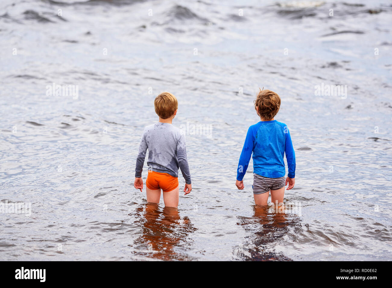 Due ragazzi in piedi ginocchio profondo nel mare, Stati Uniti Foto Stock