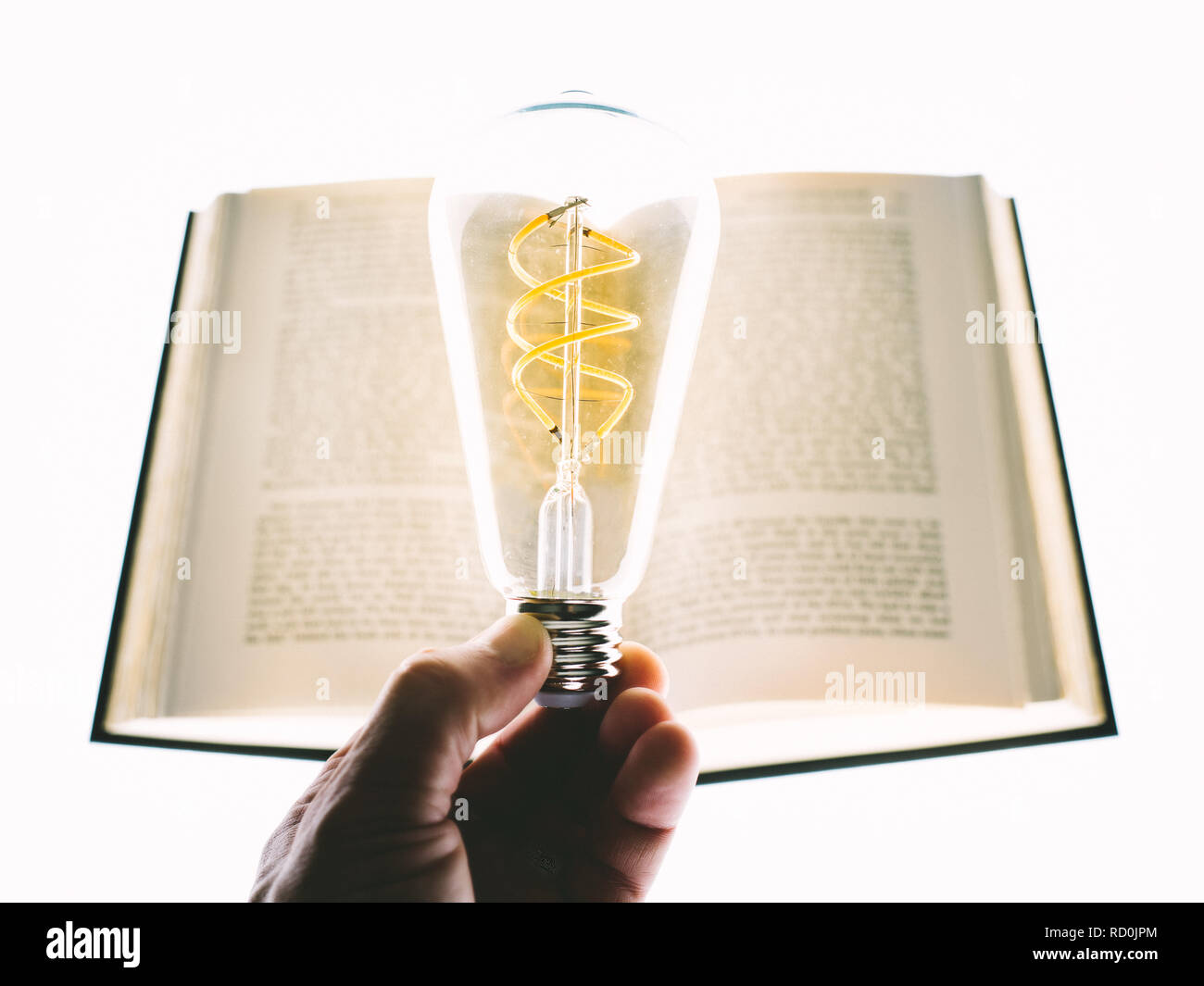 Mano umana tenendo un bulbo di luce davanti a un libro rigida Foto Stock