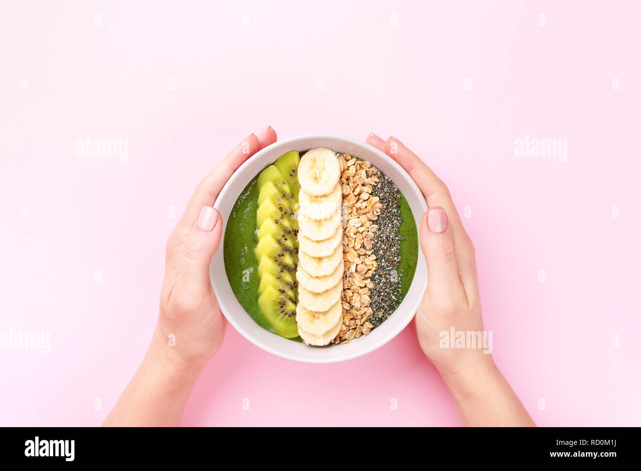 Donna di mani frullato di spinaci ciotola con muesli, quinoa, banane e kiwi su sfondo rosa. Vista dall'alto in stile minimale. Foto Stock
