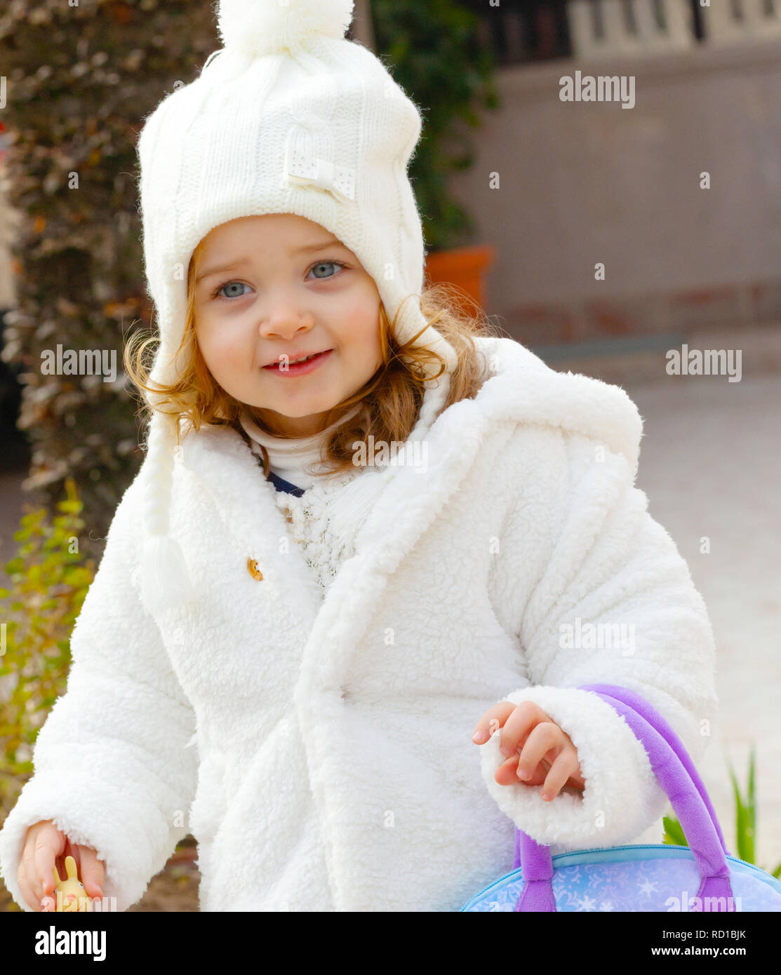 Bella ragazza con cappello di lana e e mantello bianco in un giardino in inverno. Foto Stock