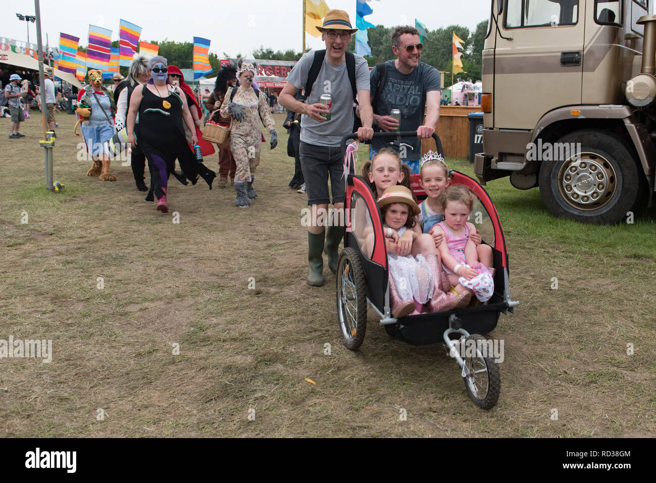Due adulti spingendo quattro figli in una a tre ruote carrello a un festival di musica Foto Stock