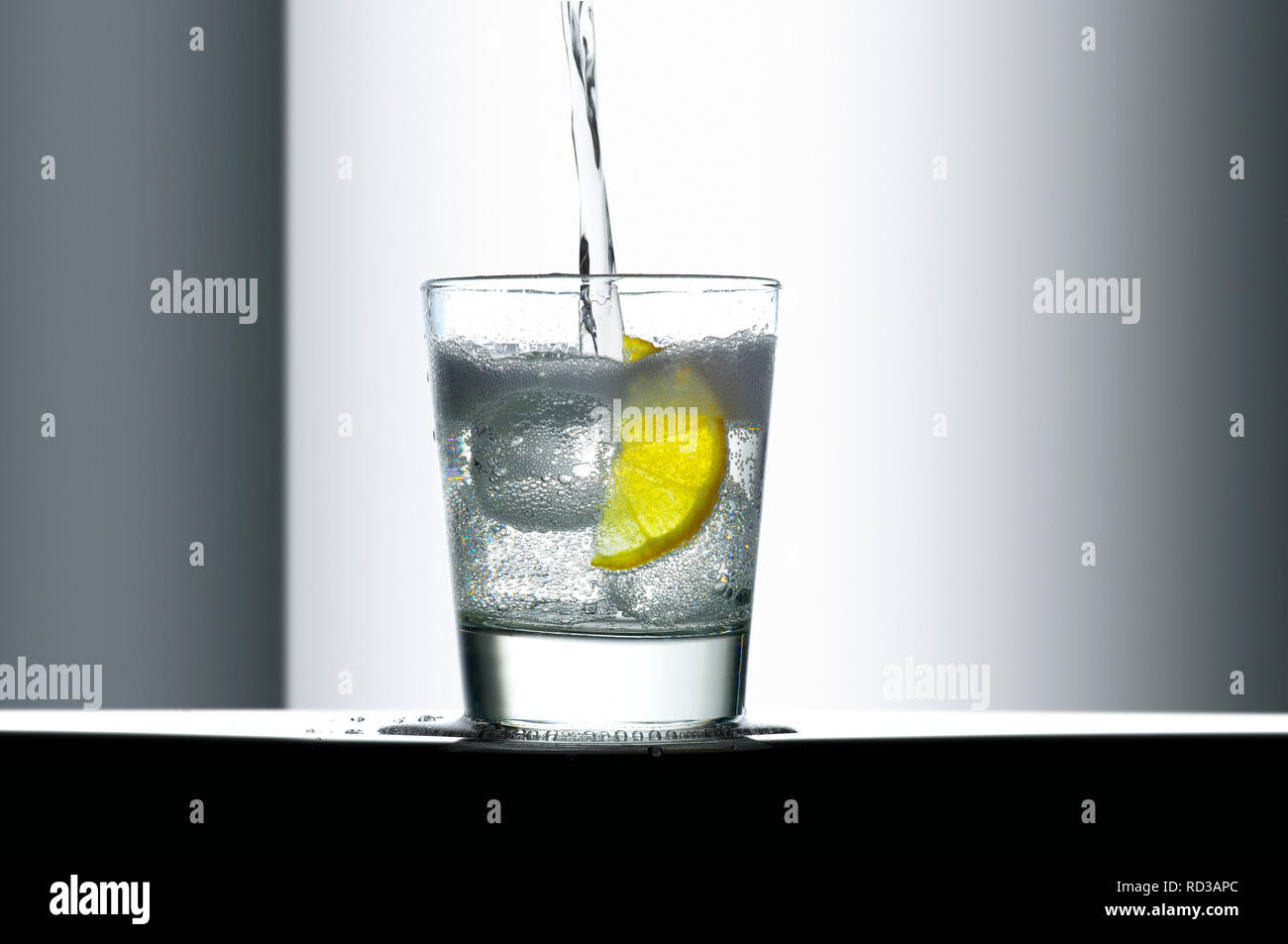 Liquido frizzante versando in un bicchiere di ghiaccio e limone Foto Stock
