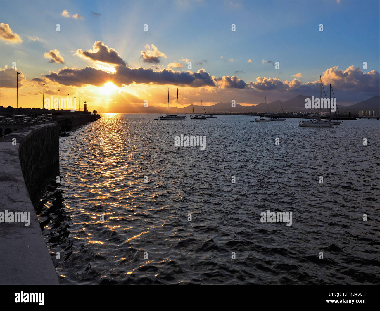 Bel tramonto con nuvole illuminato e pacifica barche a vela sull'oceano visto da una parete del mare a Arrecife, Lanzarote, Isole Canarie Foto Stock