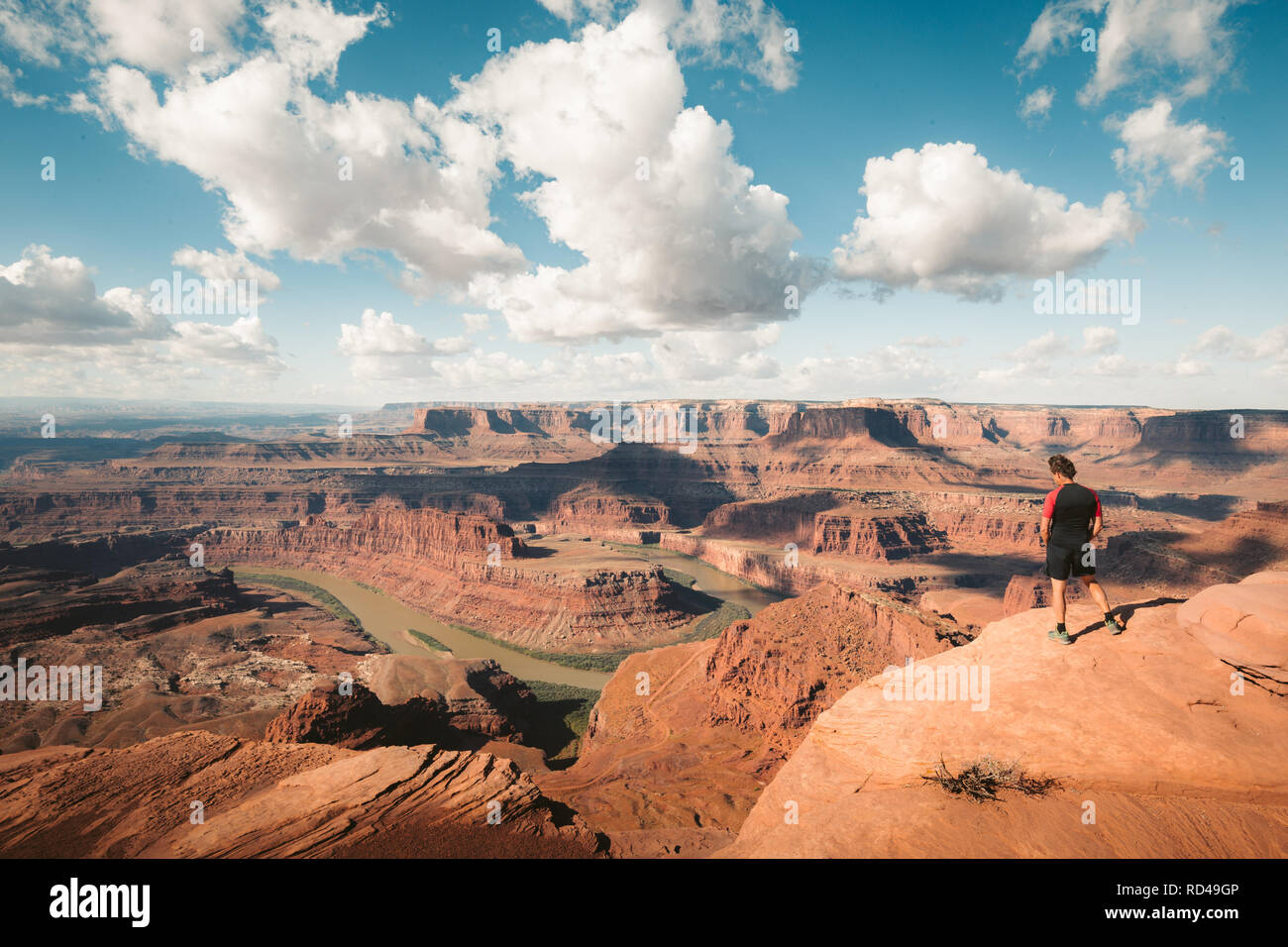 Un giovane maschio escursionista è in piedi sul bordo di una scogliera godendo di una drammatica si affacciano del famoso fiume Colorado, Dead Horse Point State Park. Utah, USA Foto Stock