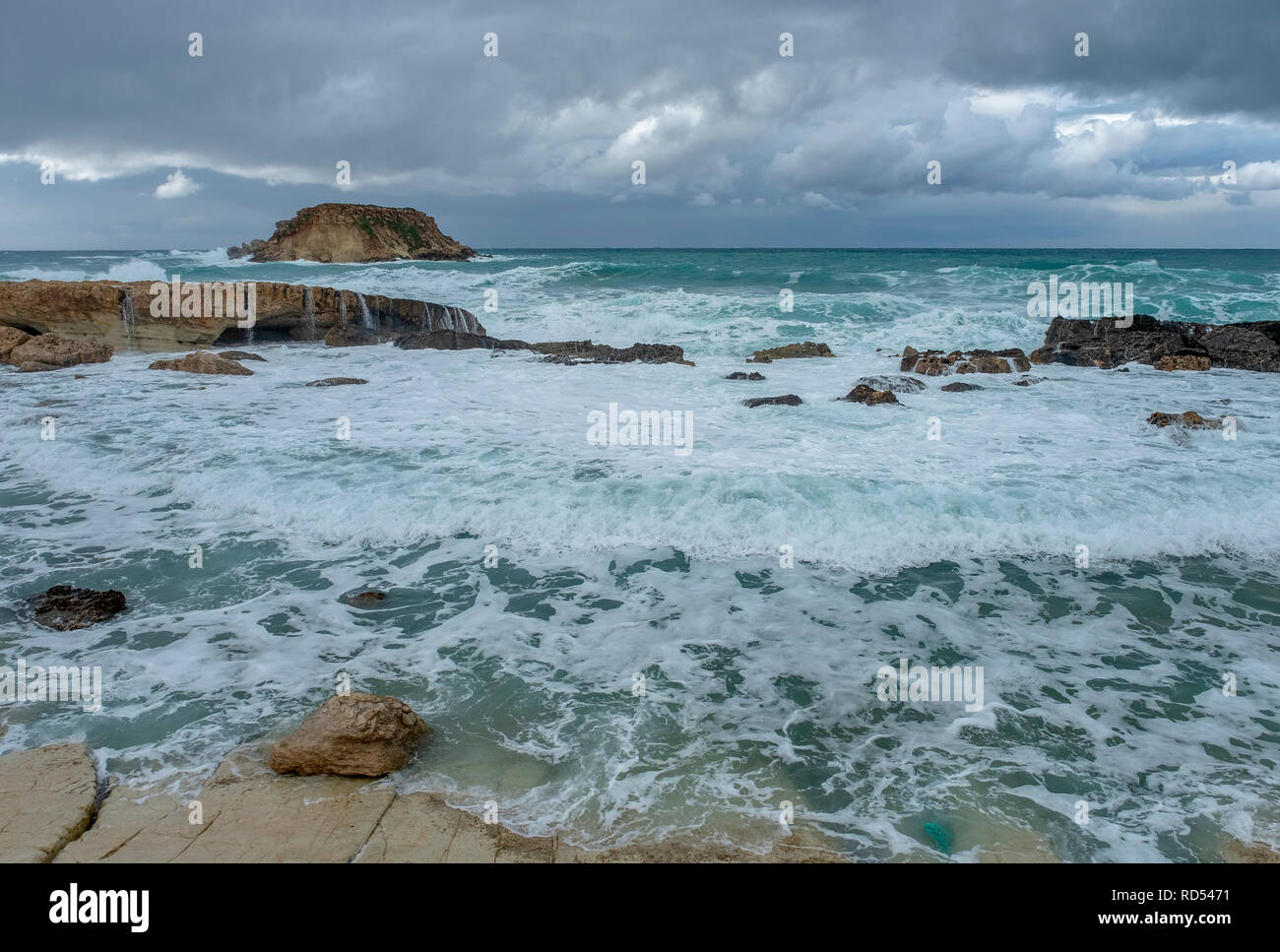 Mare mosso pastella la costa al largo di Agios Georgios, a Cipro con la piccola isola di Yeronisos dietro. Foto Stock