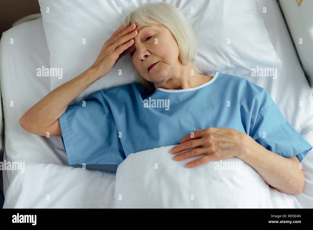 Sconvolto senior donna giaceva nel letto di ospedale, toccando la fronte e aver mal di testa Foto Stock