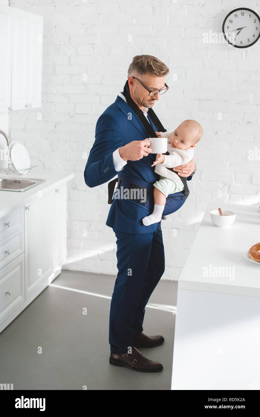 Imprenditore azienda figlia infante in baby carrier e cup con drink in mano Foto Stock