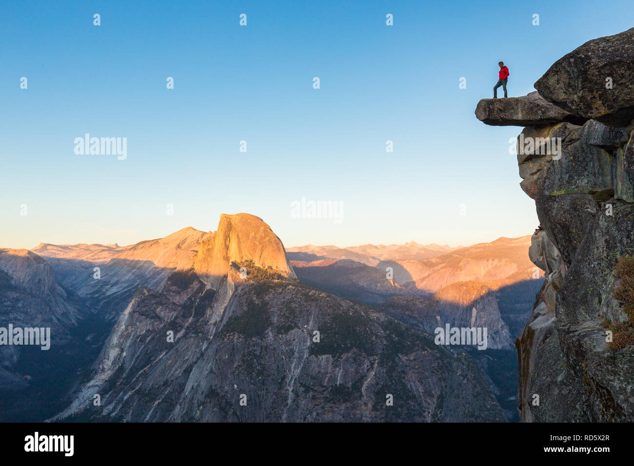 Un intrepido escursionista è in piedi su una roccia a strapiombo godendo della vista verso il famoso Half Dome presso il Glacier Point si affacciano nella bellissima crepuscolo serale Foto Stock