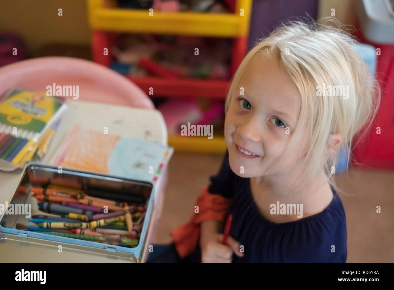 Un bambino di 5 anni bionda ragazza caucasica afferra una matita colorata mentre la colorazione e sorrisi fino alla telecamera. Stati Uniti d'America. Foto Stock