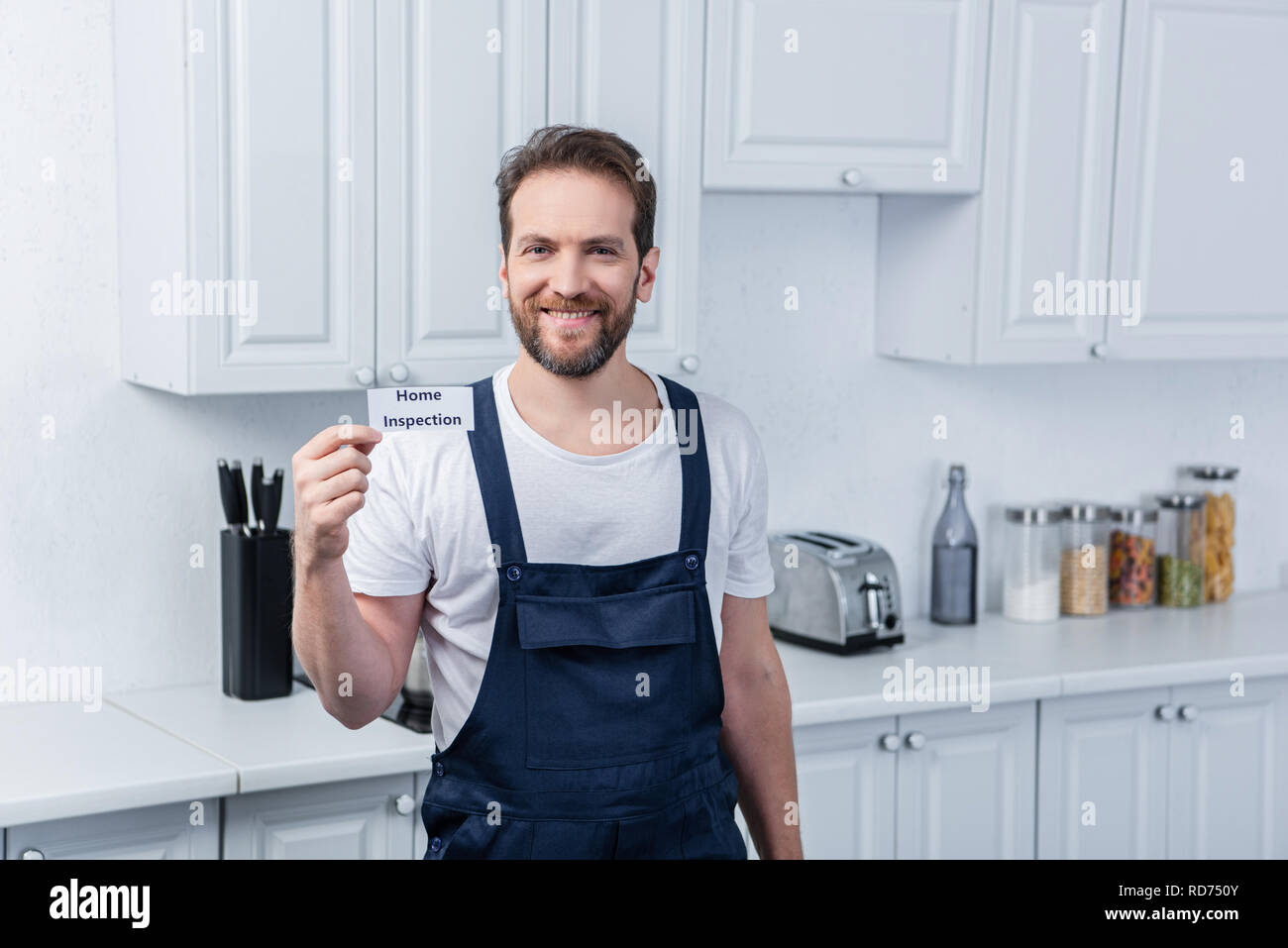 Sorridente tuttofare maschio in generale di lavoro mostra scheda con caratteri di ispezione iniziale Foto Stock