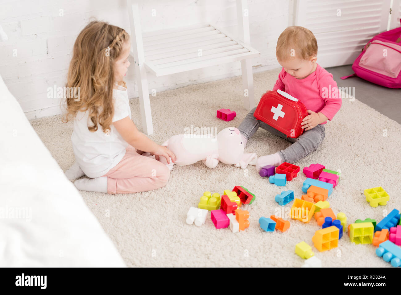 Adorabili sorelle giocando con i giocattoli sul tappeto in camera per bambini Foto Stock