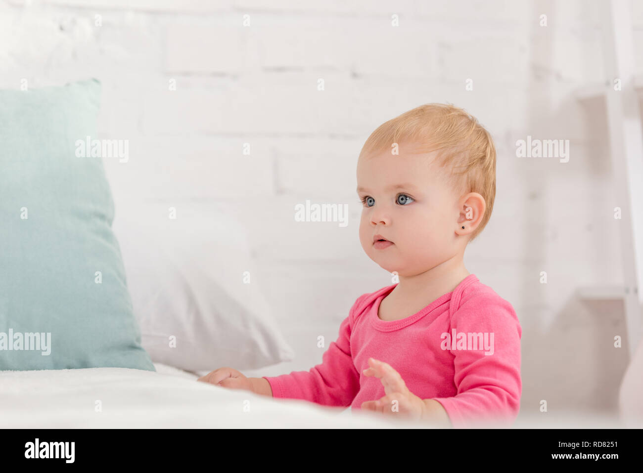 Adorable kid appoggiata sul letto e guardando lontano nella camera per bambini Foto Stock