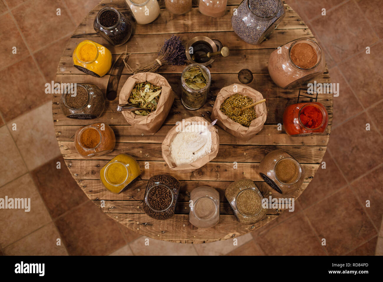 Varietà di coloratissimi le erbe aromatiche essiccate e le spezie visualizzati sul round tavolo di legno in rifiuti zero shop. Vista dall'alto di sacchetti e barattoli di vetro pieno di spezie. Foto Stock