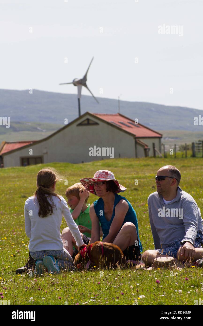 Famiglia rilassante godendo la visione di sport competitivo come parte del Festival Berneray taing posto sulla fioritura machir , precedentemente in estate habitat di nidificazione di poco sterne . Sala comunitaria del Borve dietro con fonti di energia rinnovabili turbina eolica . Foto Stock