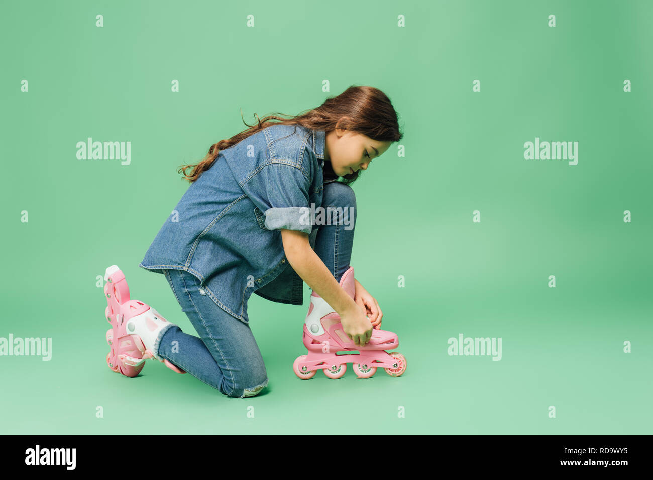 Bambino in denim mettendo sul rullo le lame su sfondo verde Foto Stock