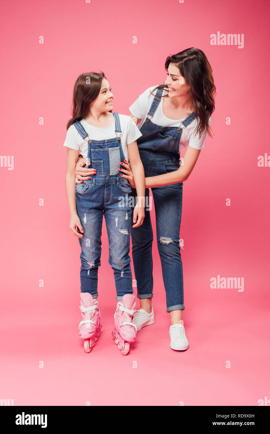 Sorridente madre abbracciando la figlia di lame a rullo su sfondo rosa Foto Stock