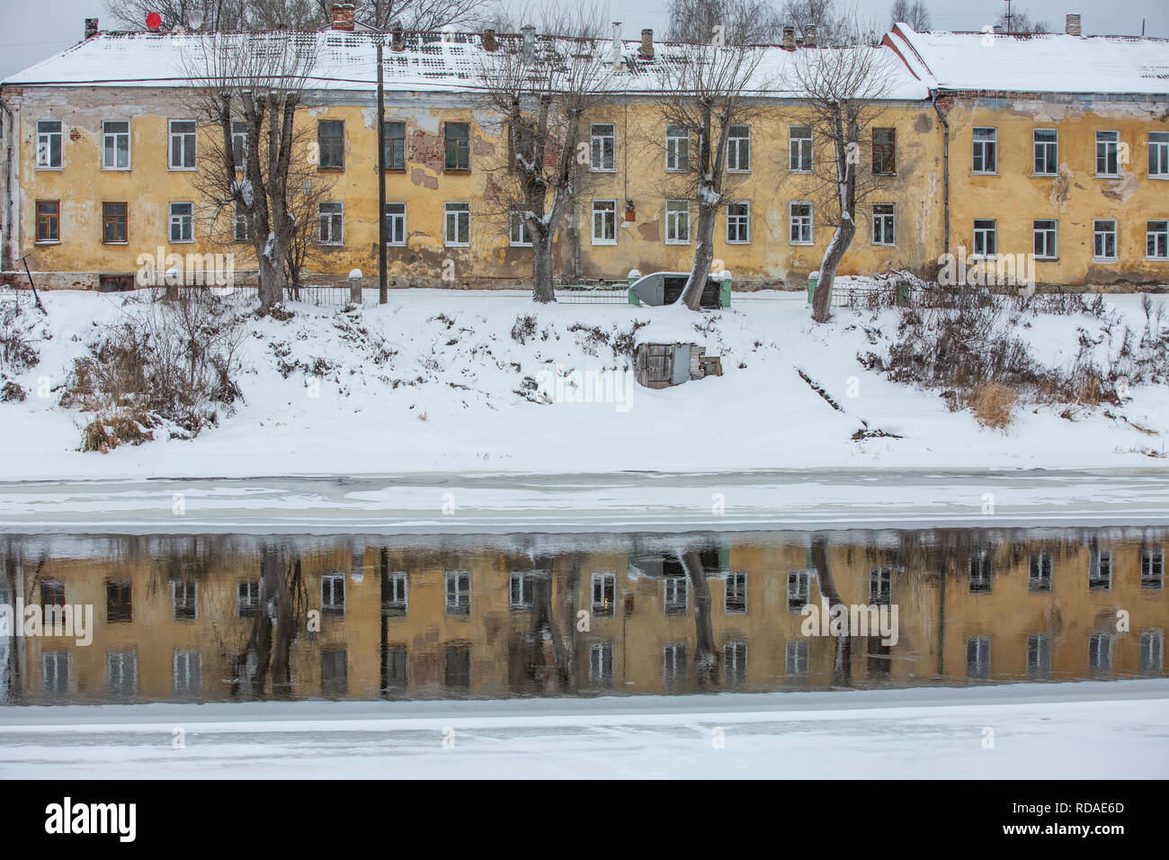 Il vecchio edificio di colore giallo sulla costa del fiume e la sua riflessione in justr acqua congelata Foto Stock