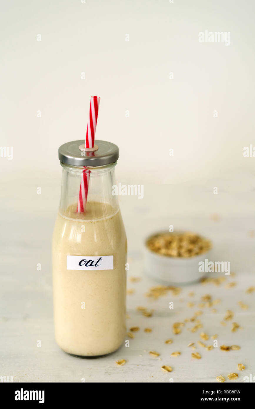 Bottiglia di vetro di latte di avena su sfondo bianco. Ciotola con fiocchi di avena vicino ad essa Foto Stock