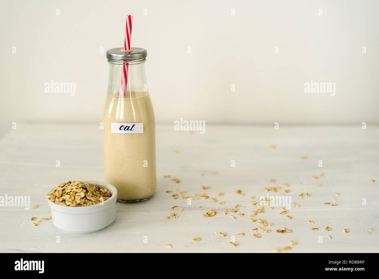 Bottiglia di vetro di latte di avena su sfondo bianco. Ciotola con fiocchi di avena vicino ad essa Foto Stock